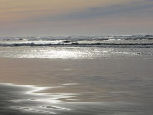 A photograph of Ocean Shores, Washington, depicting ocean waves and shallow water on a cold, cloudy day.