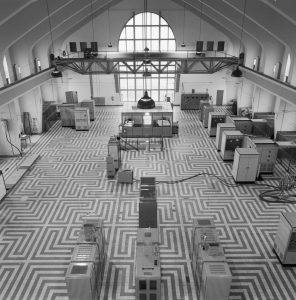 Black-and-white photograph of a cavernous room with high arches and maze-shaped carpeting.