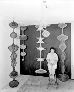 Ruth Asawa sitting amongst her wire sculptures