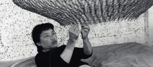 Ruth Asawa underneath a looped wire sculpture, adding in another layer of wire
