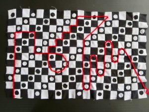 Black and white patchwork textile with repeating checkerboard pattern. Red angular and curving line design