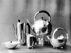 A black-and-white photo of a set of brass coffee pots and tea pots set against a dark background.