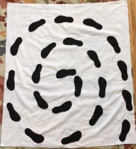This is a spiral of black footsteps sewn onto a white cloth, resembling a labyrinth