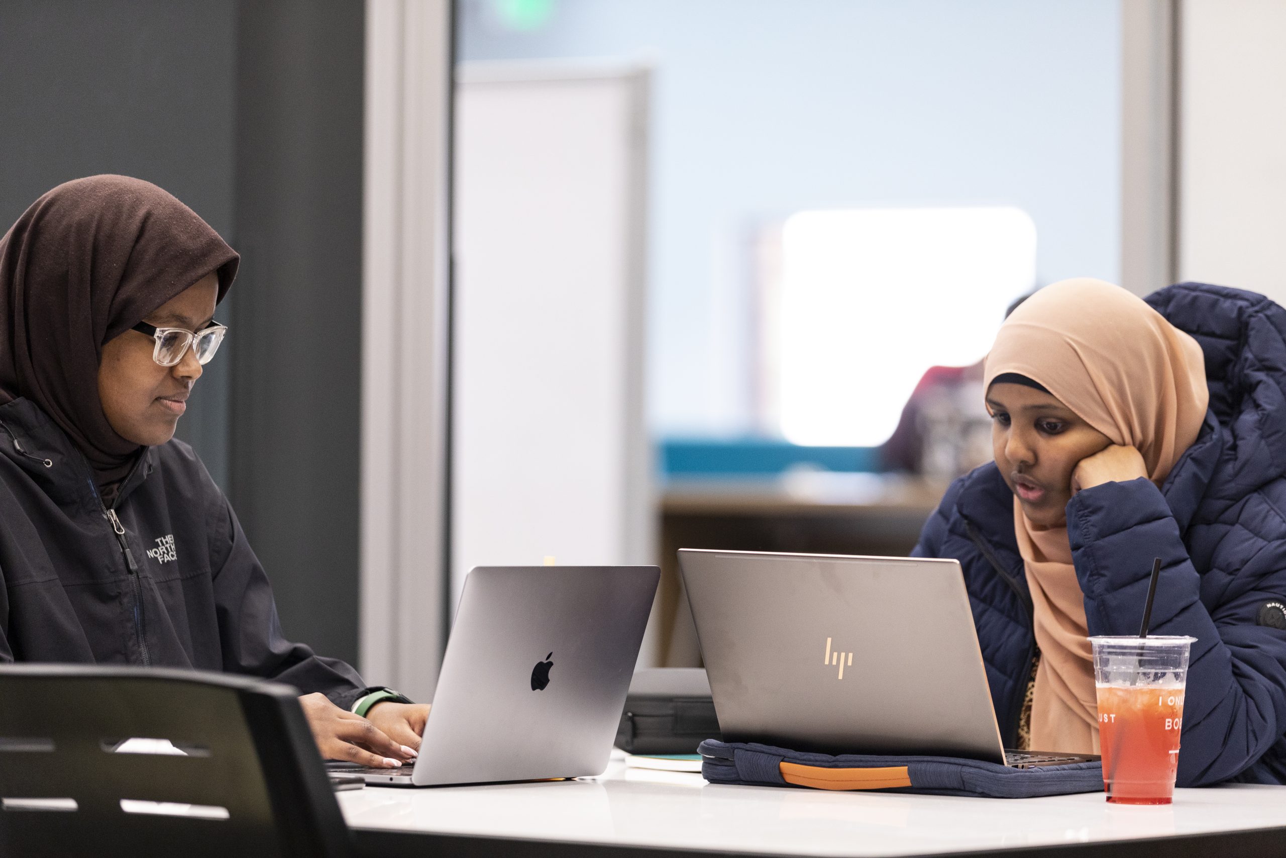 Two female students wearing hijabs working on laptops.