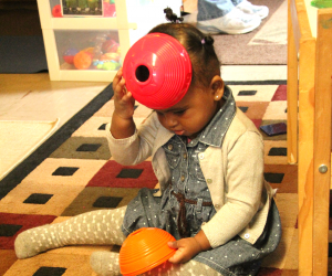 Toddler putting a bowl on her head like a cap