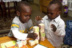 Two toddlers trying to prevent a stack of blocks from falling