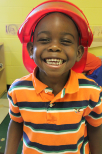 Child smiling broadly while wearing a play fireman's hat