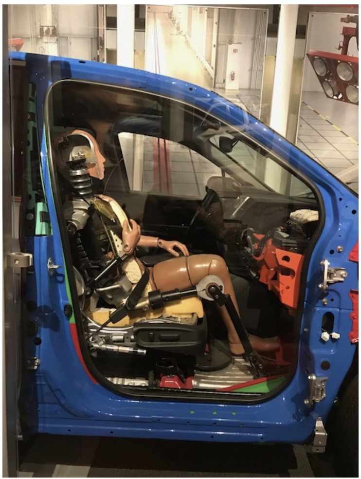 A crash test dummy sitting in a car with the side door removed