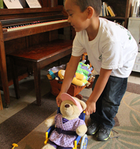 young boy pushing a stuffed bear who is in a wheelchair