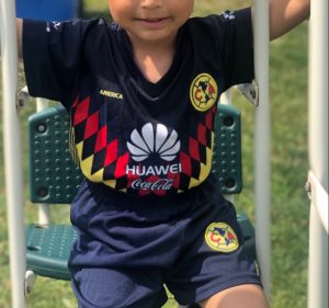 Young boy dressed in Club América soccer gear on an outside green swing