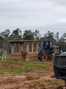 Seabees in a field environment constructing a timber guard shack with the aid of a front-end loader.