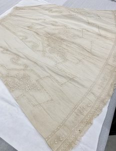 An image of the piña cloth skirt laid out on a table. Intricate designs and woven patterns can be seen in the beige colored fabric.