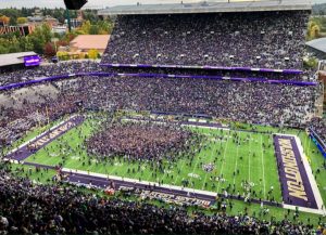 A wide shot of a football field. The stands are packed with people, and the field is full of people.