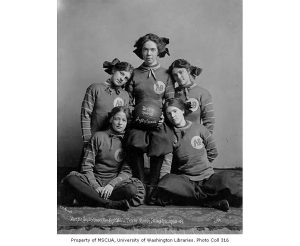 This is a black-and-white photograph of five women from the Arctic Sisterhood Basketball Team in Nome, Alaska, taken around 1908-1909, all dressed in matching uniforms with 'AB' initials on their tops, posing together in a studio setting.