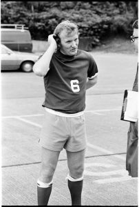 A Seattle soccer player being interviewed, standing outdoors with a calm expression, holding a soccer ball in front of them.