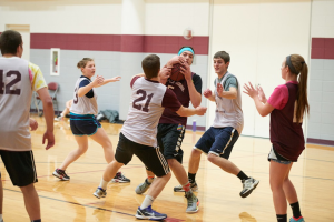 Male and female basketball players in jerseys fight over a ball on a basketball court.