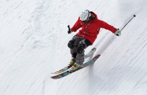 This picture shows a skier in a red coat and helmet in action skiing down a snow-covered slope.