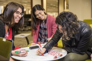 Three students gathered around a whiteboard table