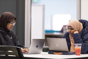 Two female students wearing hijabs working on laptops.